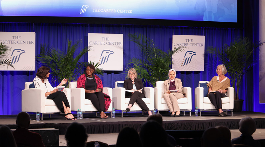 five women sit in white chairs on a stage